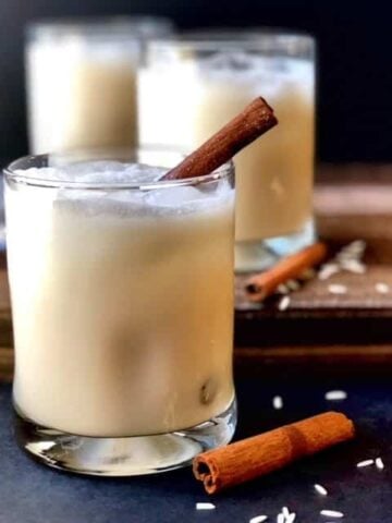 Mexican Horchata in glasses with cinnamon sticks in them. They are sitting on a black surface