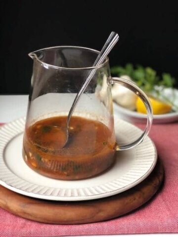 Red chimichurri in a glass container on a white plate.