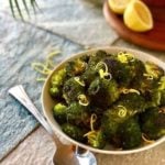 broccoli in a bowl on a stone surface with a spoon next to it