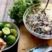 cole slaw in a bowl with a bowl of limes and cilantro next to it