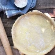 Pie crust in a pie pan on wood board with a rolling pin and flour next to it