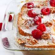 French toast casserole in glass baking dish with powdered sugar and berries on top.