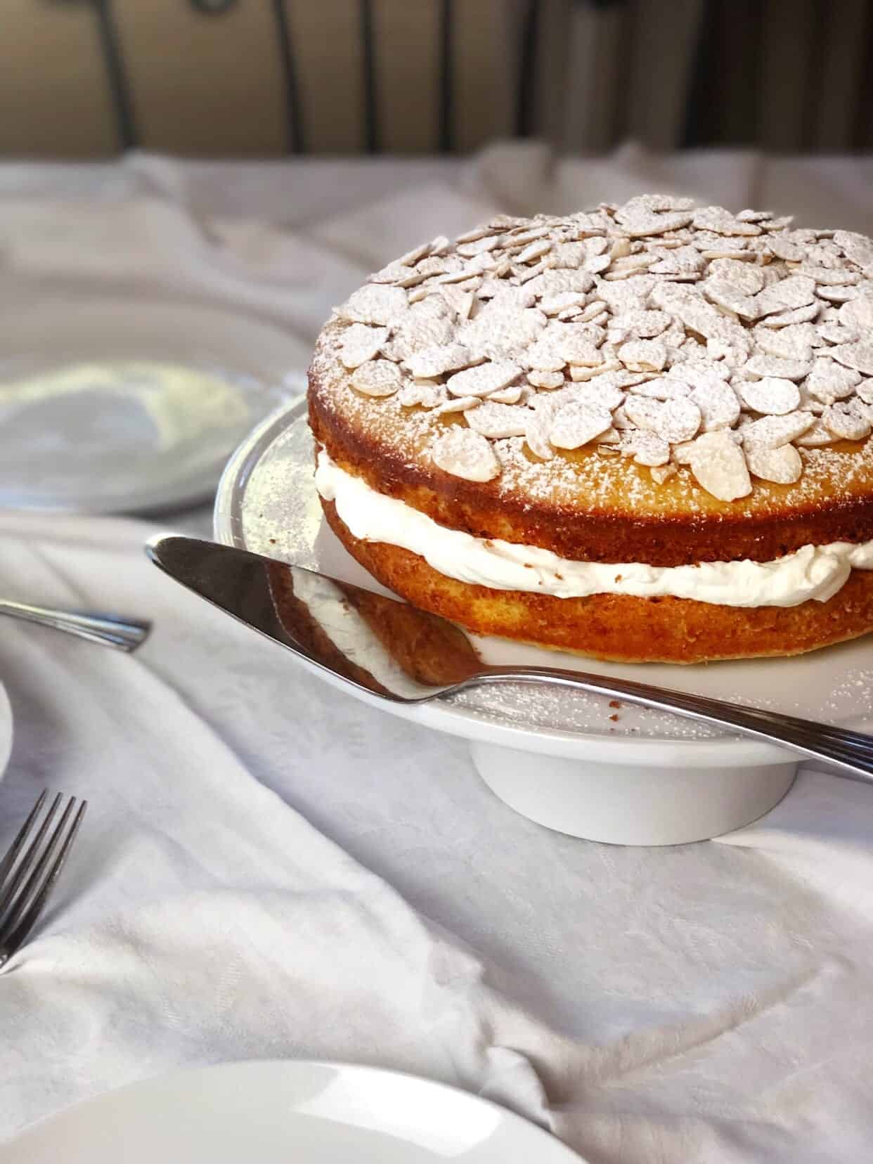 Vanilla almond layer cake on a cake stand with a serving spatula next to it.