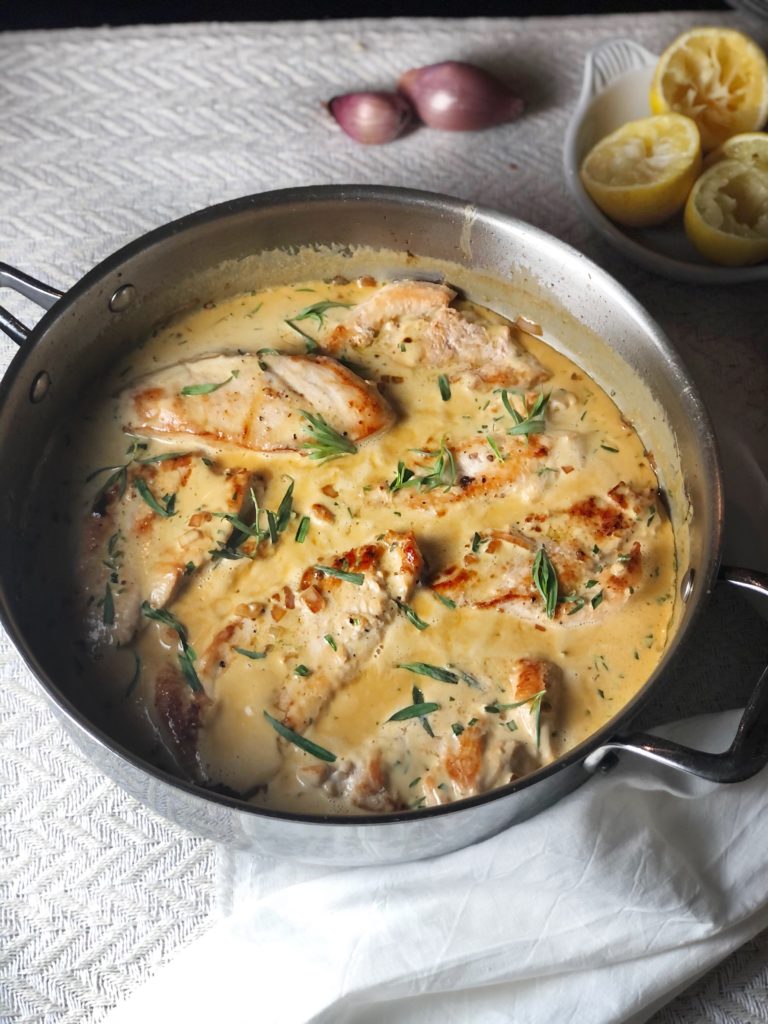 creamy tarragon chicken in a pan with lemons in the background