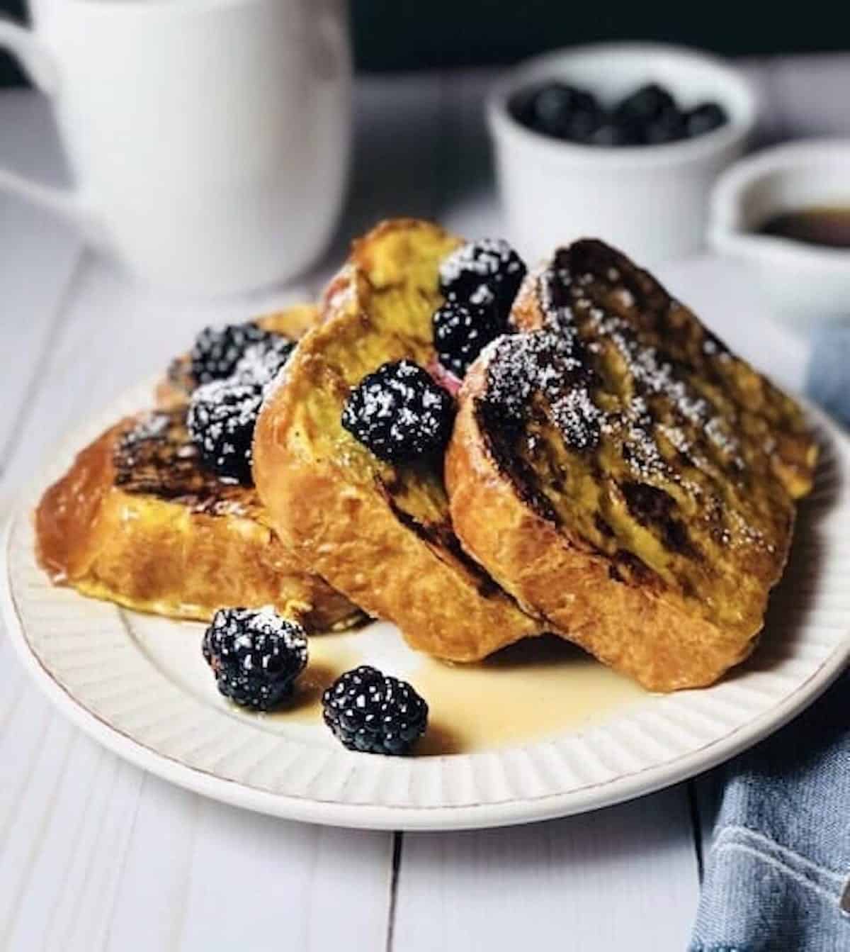 Brioche French toast on a plate with honey and blackberries on top.