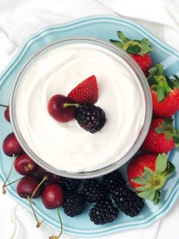A small glass bowl of dip surrounded by fruit