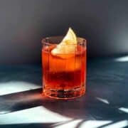 Aperol and soda in glass with a lemon wedge on a blue counter