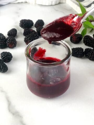 closeup of blackberry puree being poured off of spoon into a bowl