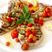 grilled pork chops on plate with tomatoes on top