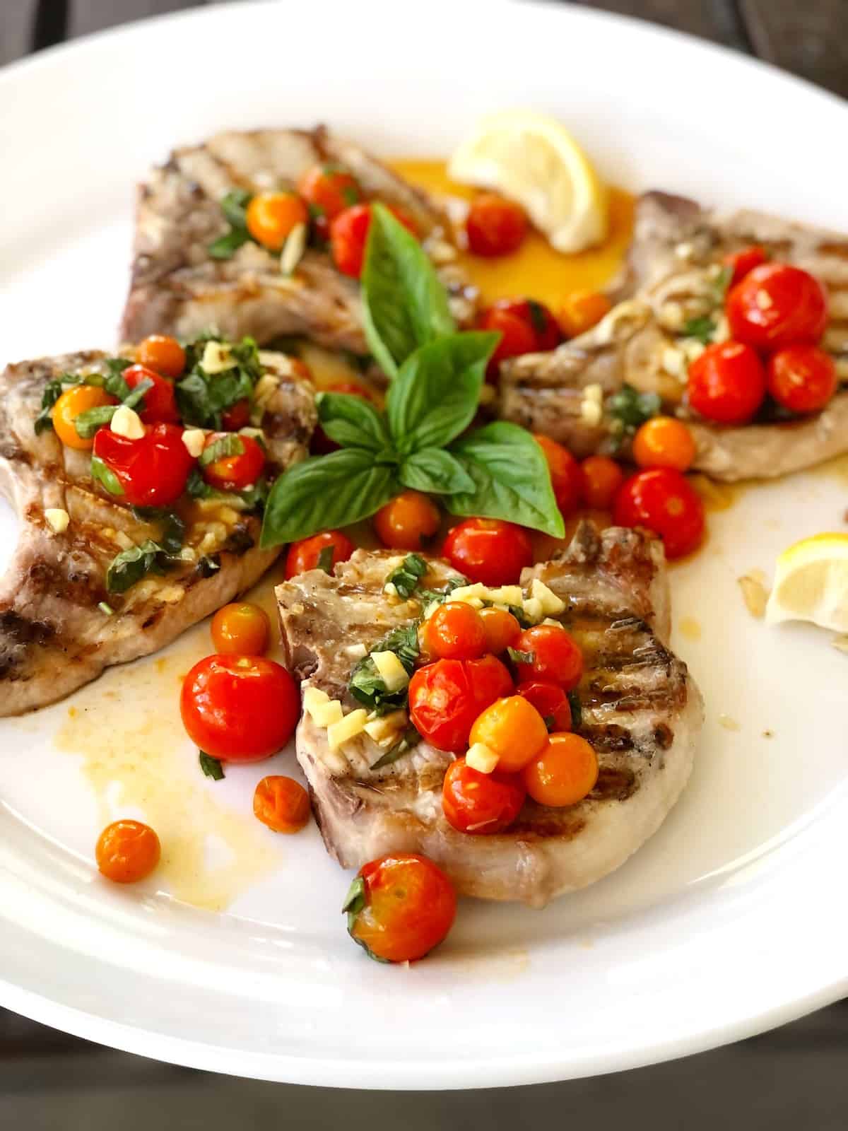 grilled pork chops on plate with tomatoes on top