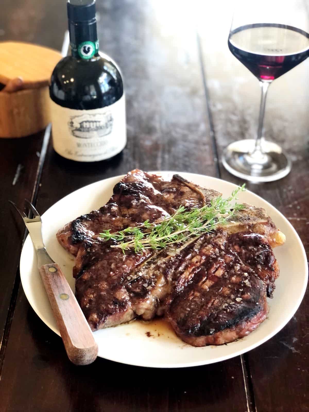 t bone steak on a plate on table with wine in background