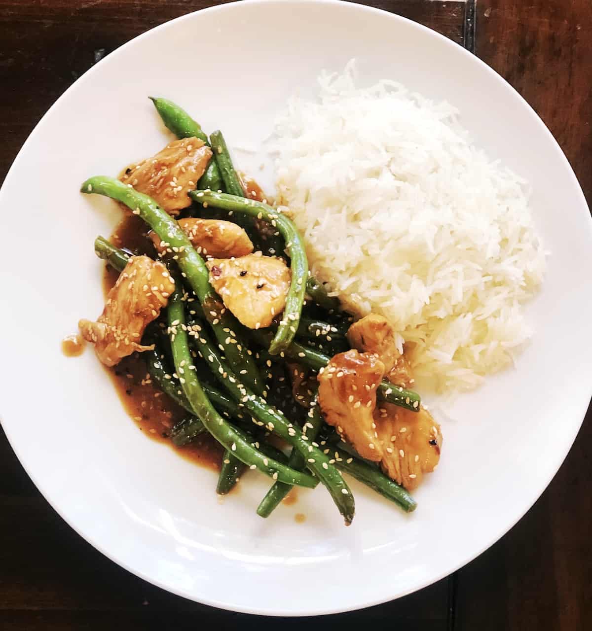 A white plate topped with rice chicken and green beans.