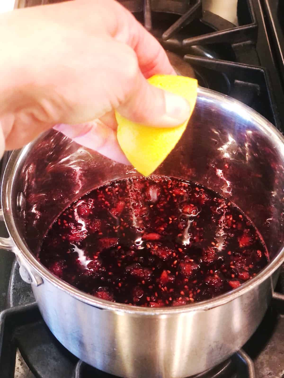 A person squeezing lemon into a pot of blackberry syrup.