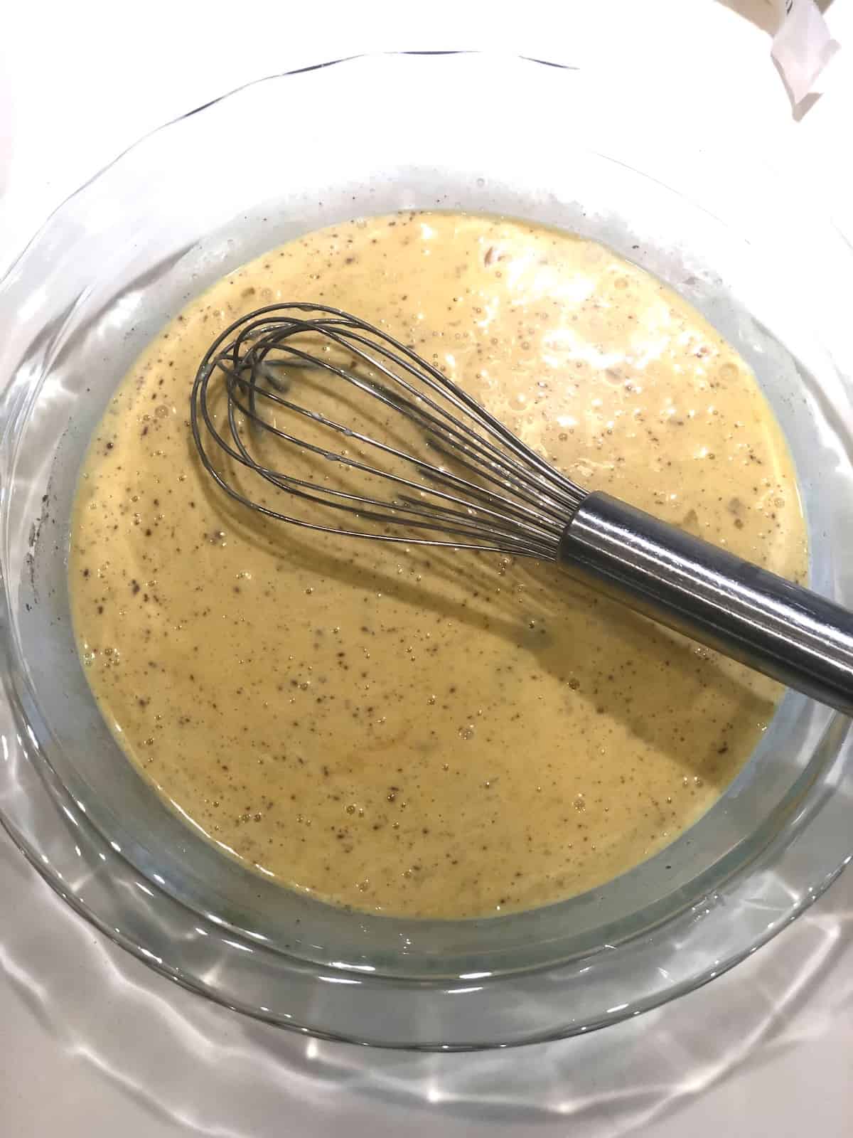 A bowl of custard with a whisk in it.