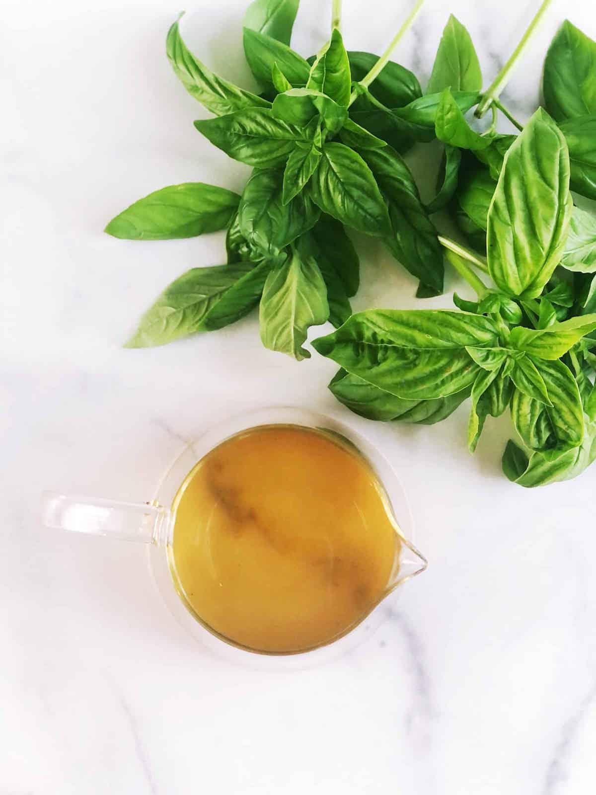 A glass of simple syrup with basil leaves next to it.