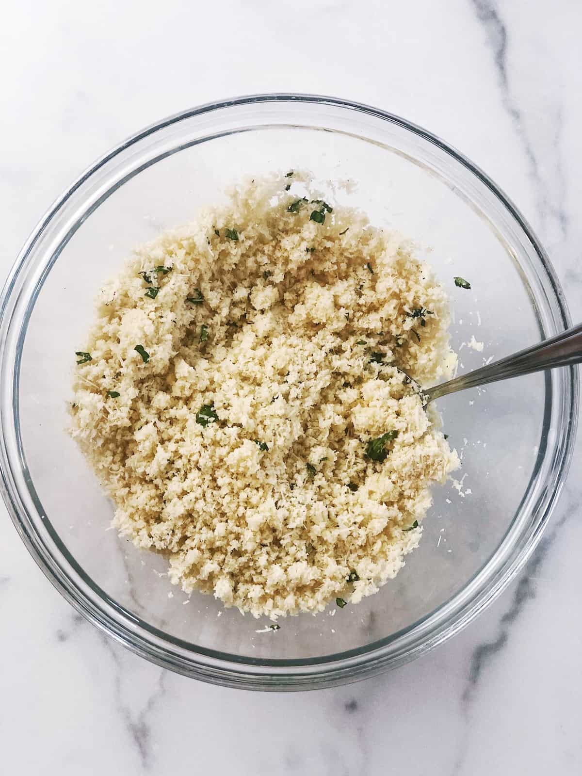 Breadcrumbs in a glass bowl with a spoon.