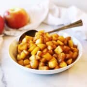 A white bowl with apples and a spoon.