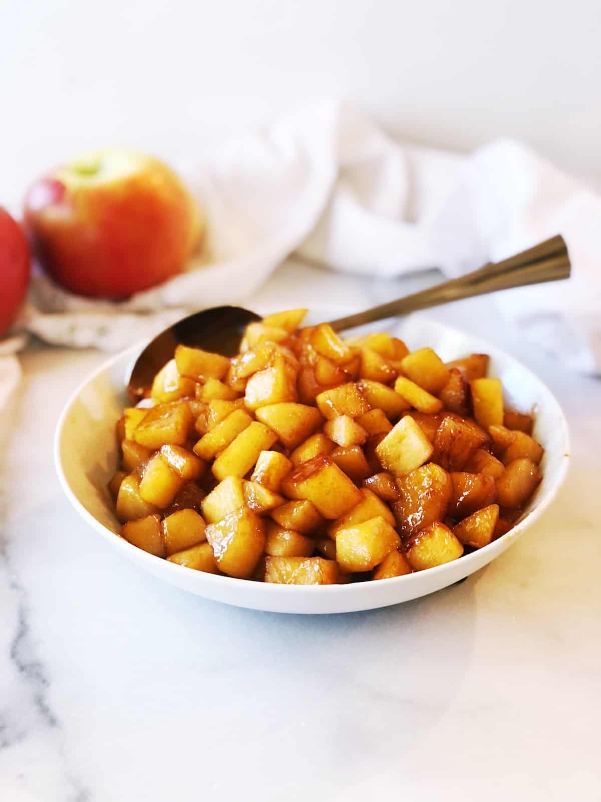 A white bowl with apples and a spoon.