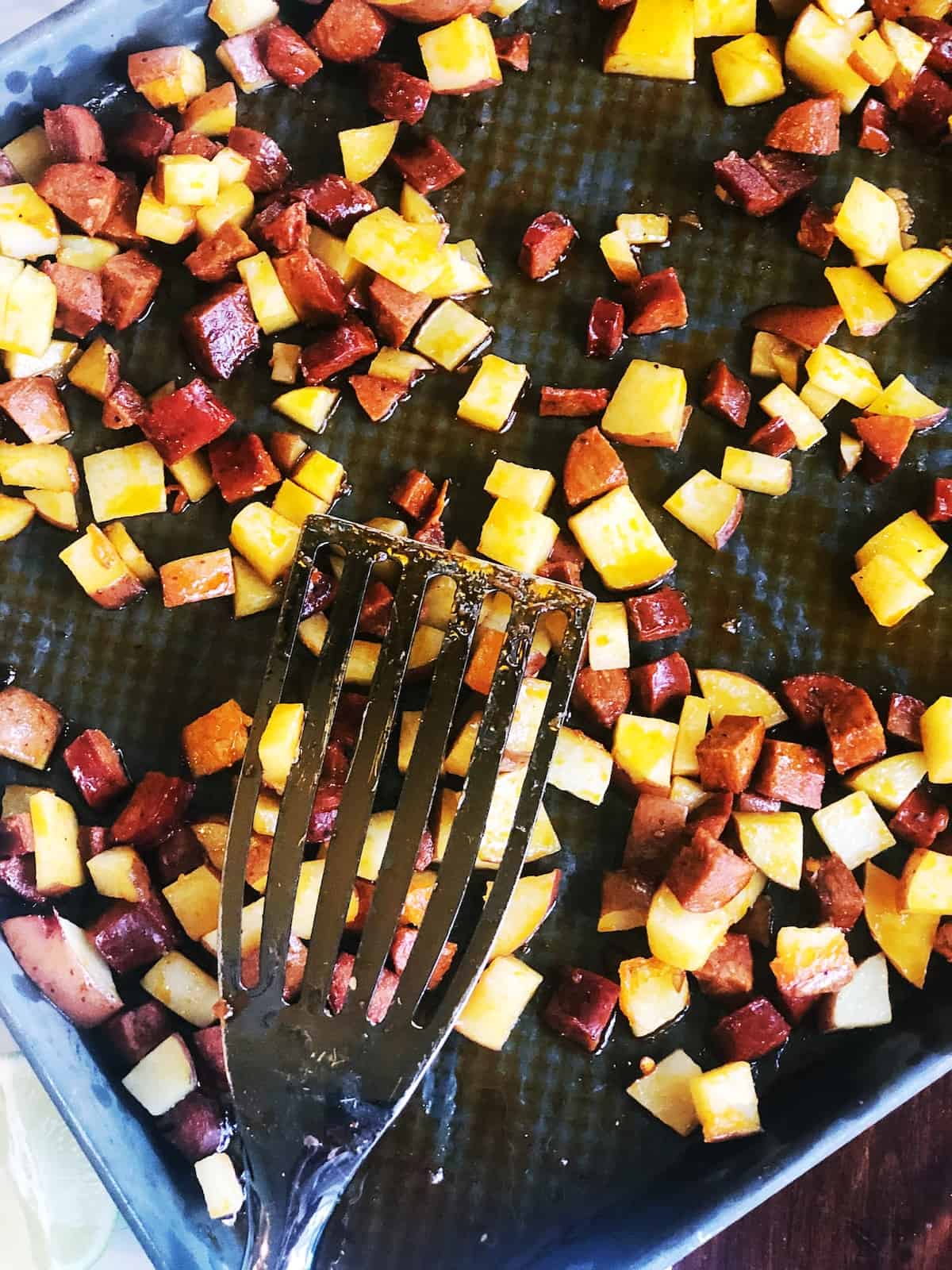 A baking sheet with chorizo and potatoes and a fork on top of it.
