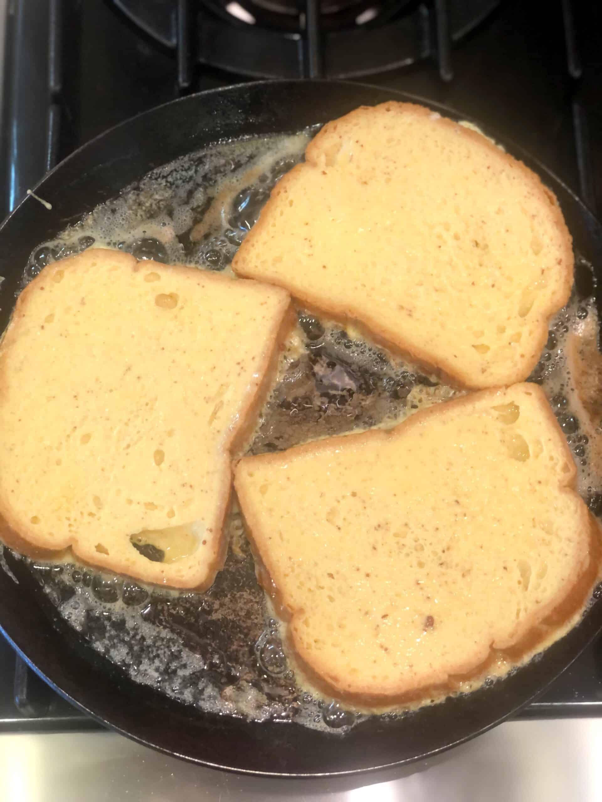 Three pieces of French toast are being cooked in a pan on a stove.