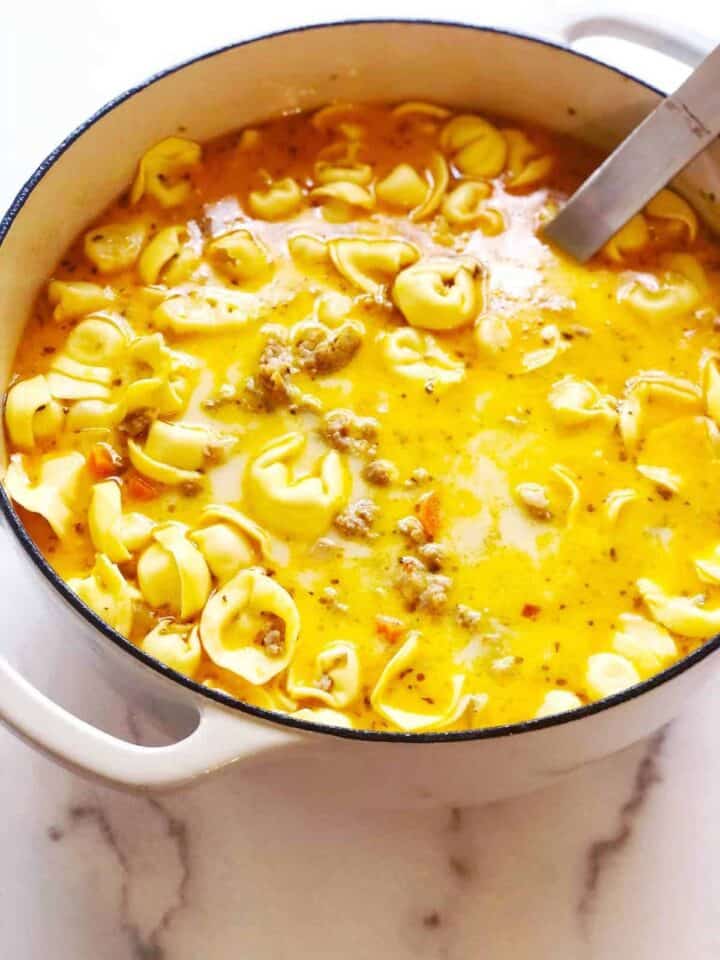 Tortellini soup in a white pot with a spoon.
