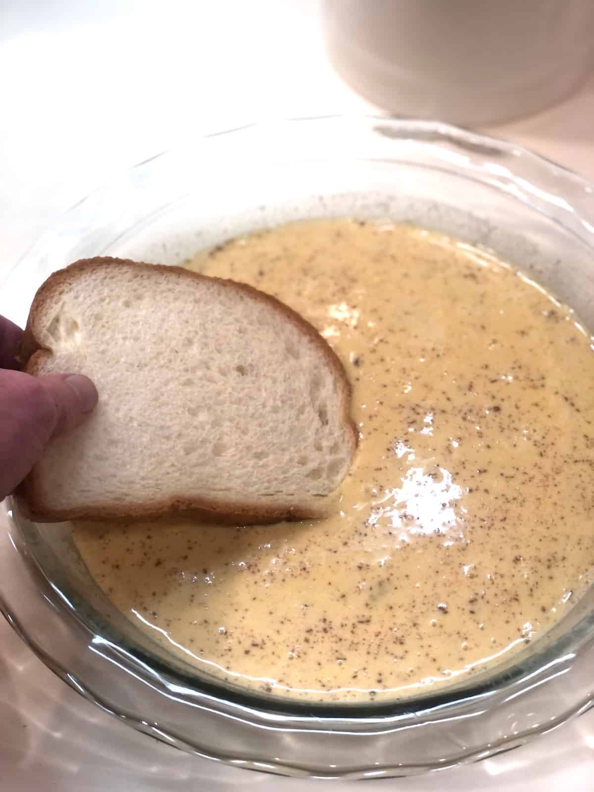 A person is dipping bread into a bowl of French toast custard.
