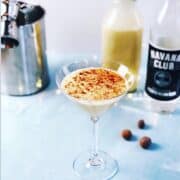 An eggnog martini in a glass next to a bottle of liquor.