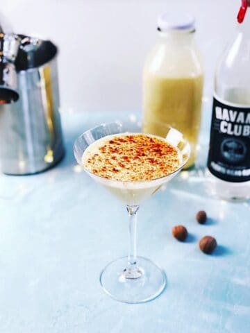 An eggnog martini in a glass next to a bottle of liquor.