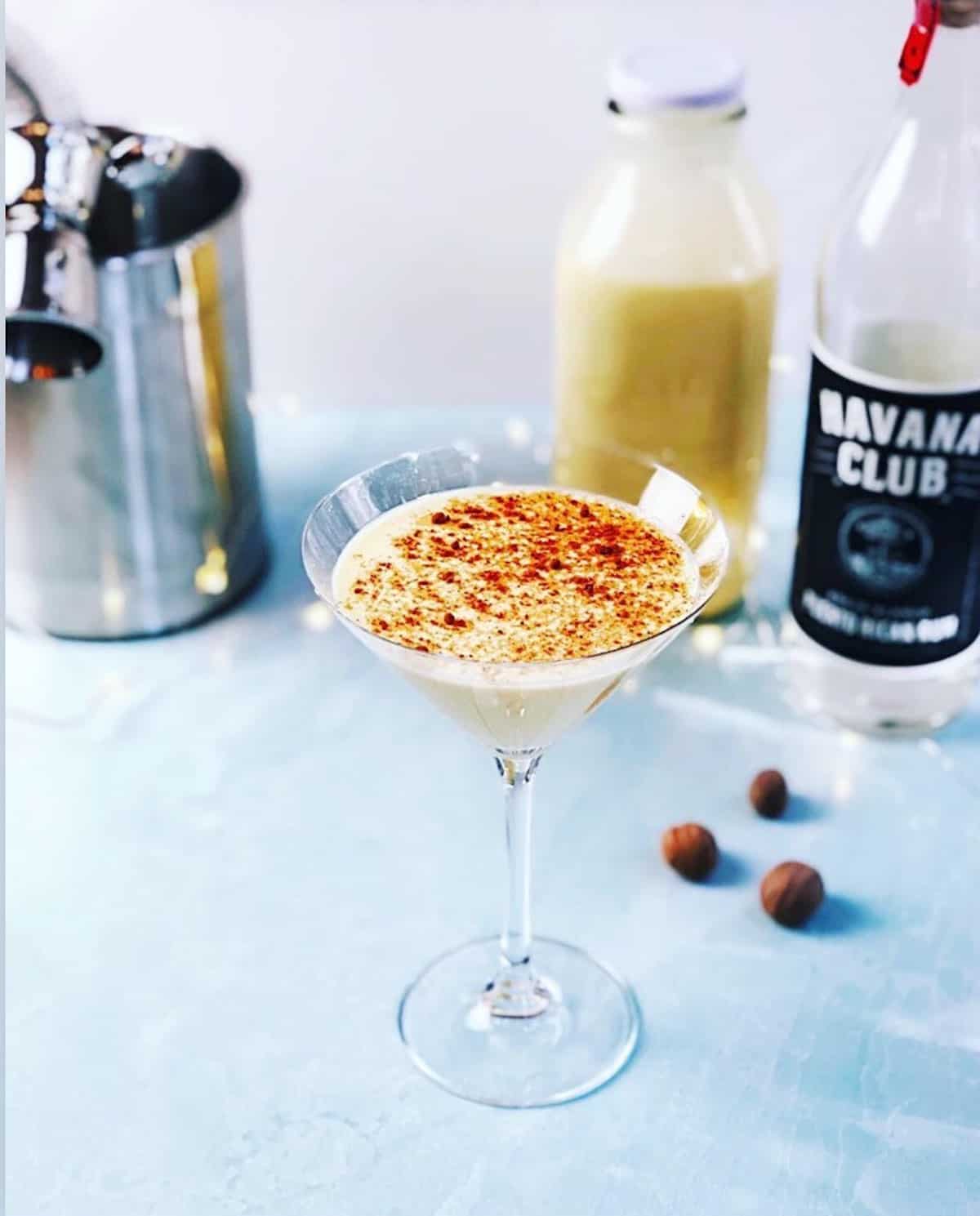 An eggnog martini in a glass next to a bottle of liquor.