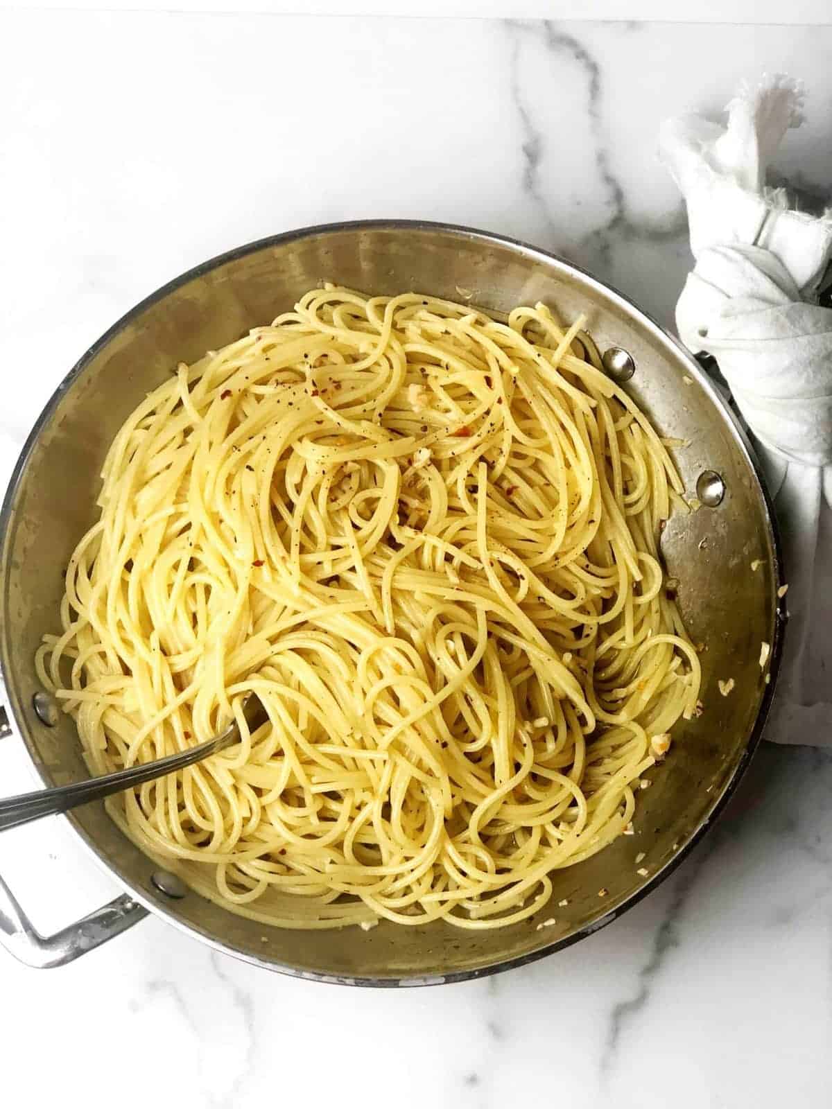A pan full of spaghetti on a marble countertop.
