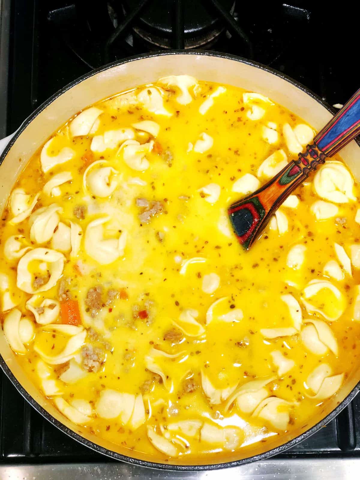 Tortellini soup in a pot on a stove.