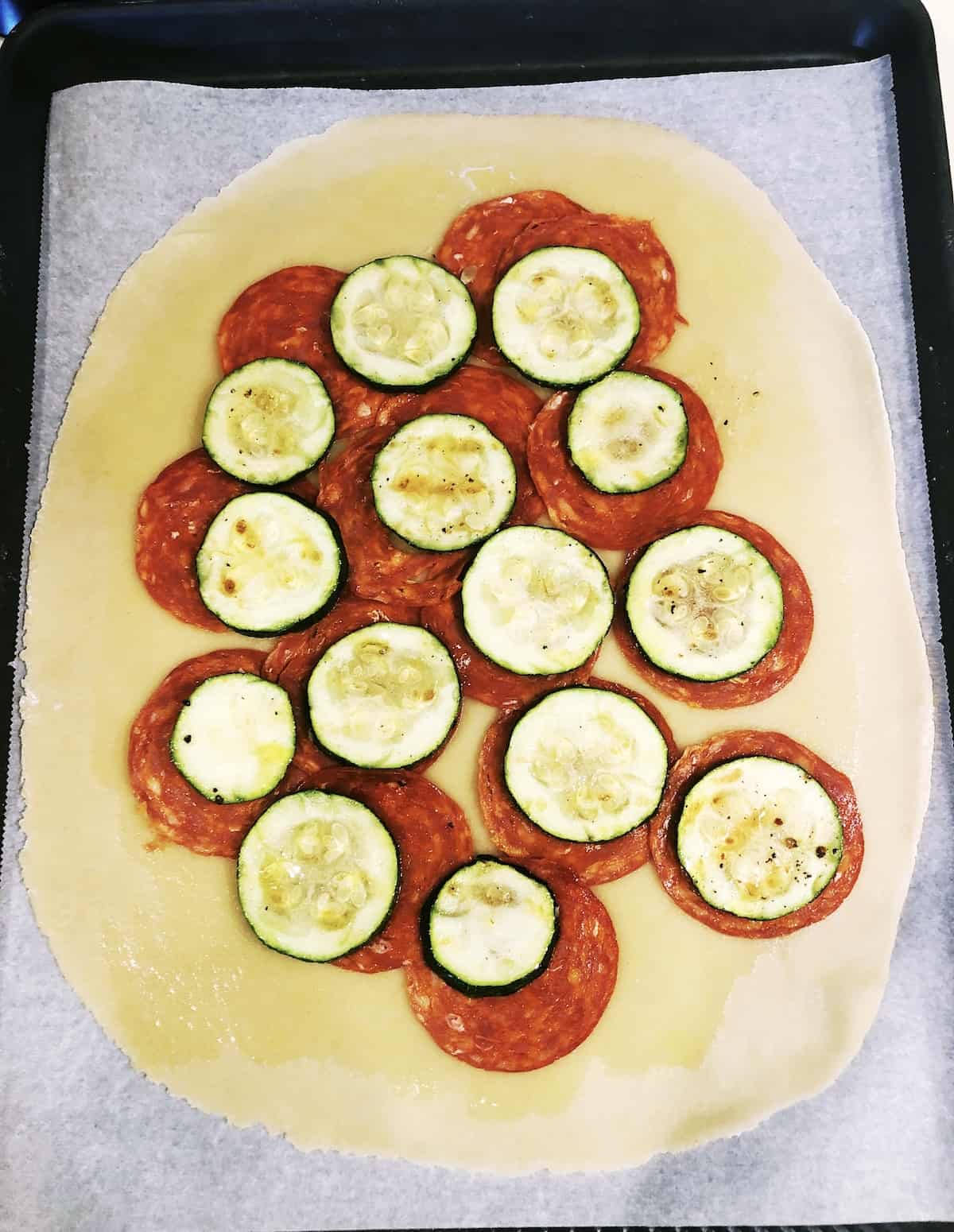 A galette with chorizo and zucchini slices on a baking sheet.