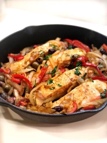 A skillet with Mediterranean salmon, onions and peppers.