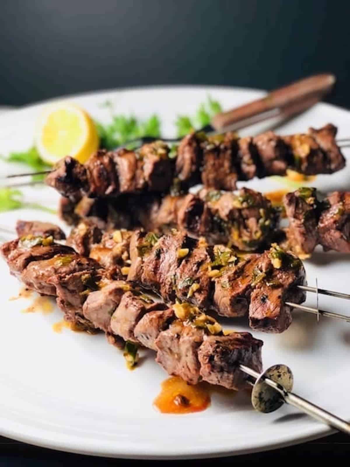 Grilled steak tips on skewers on a white plate.