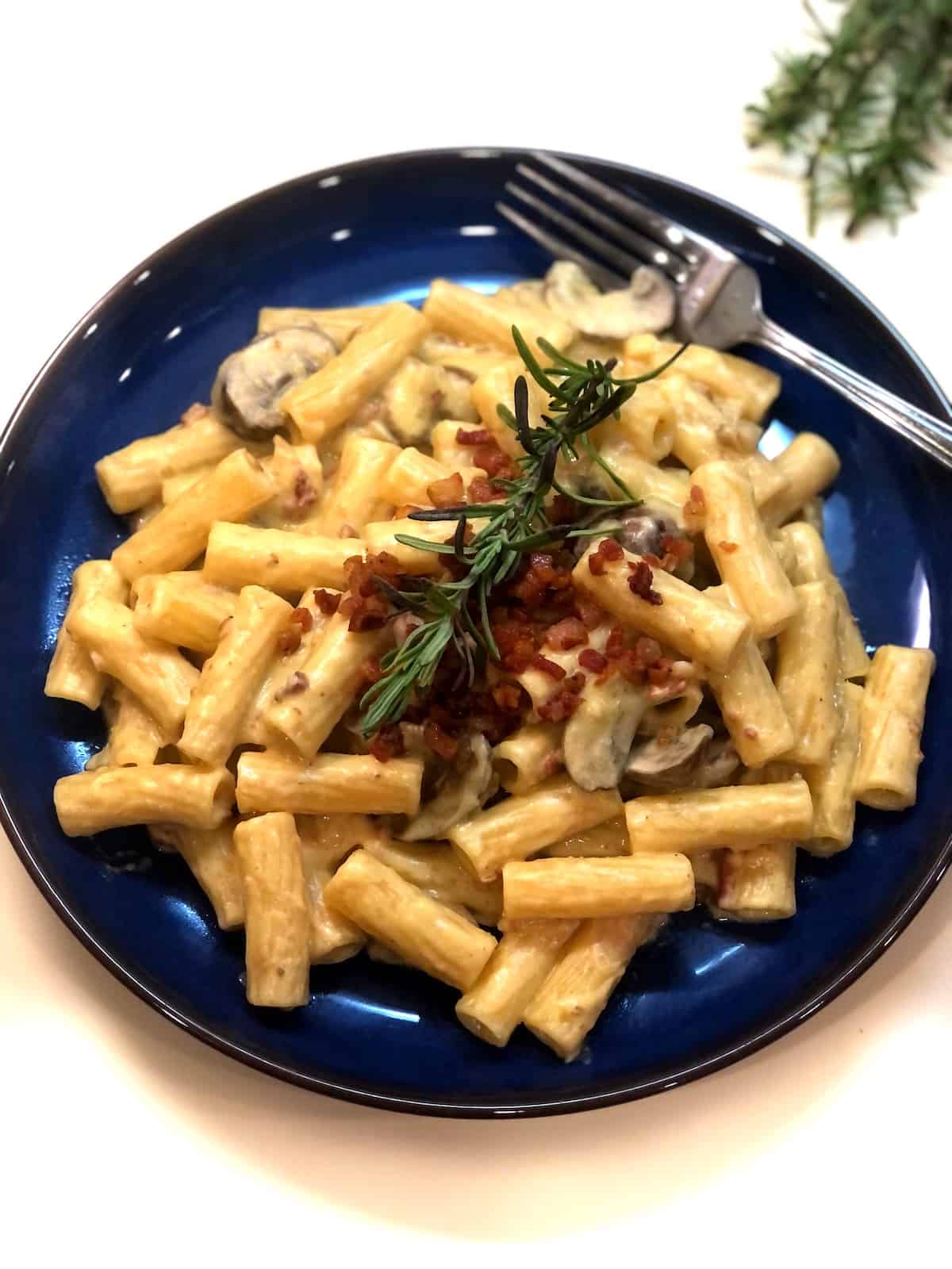 Acorn squash pasta with mushrooms and bacon on a blue plate.