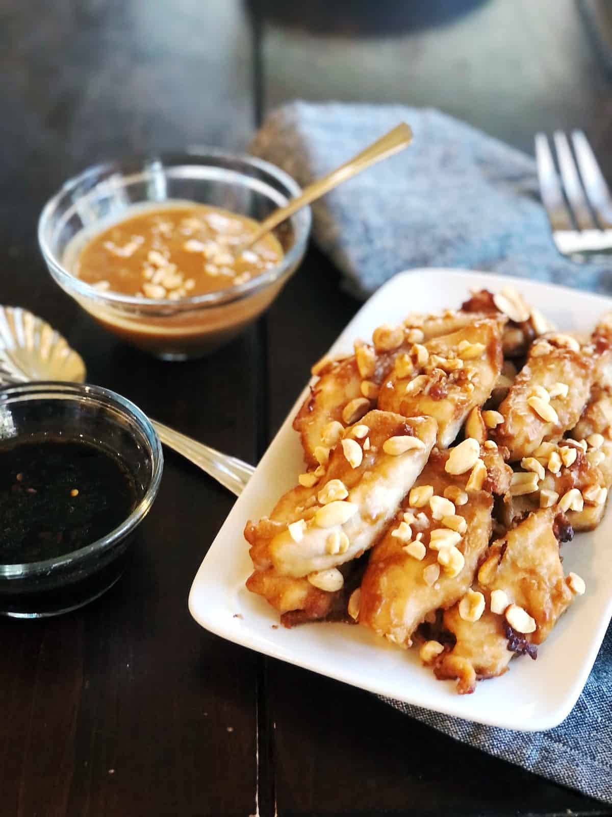 Baked chicken satay with peanut sauce on a white plate.