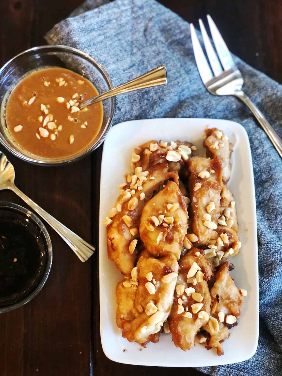 Baked chicken satay without skewers with peanut sauce on a white plate.
