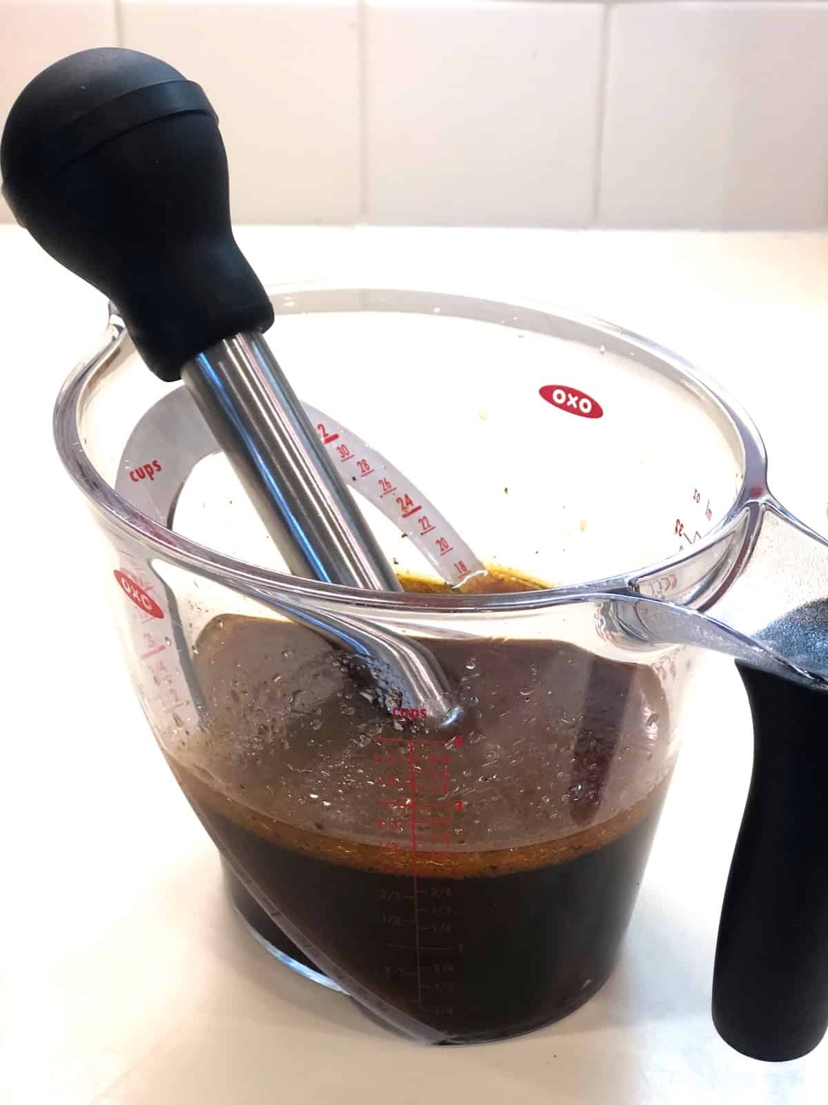 A measuring cup with pan drippings and spoon in it.