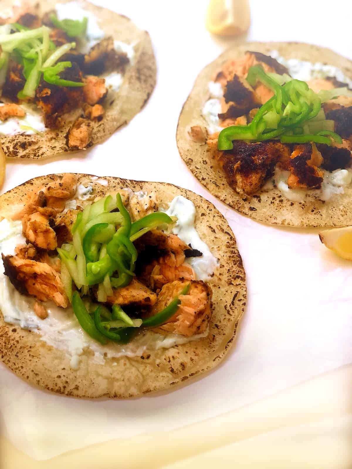 Blackened salmon tacos with yogurt sauce and lemon wedges.