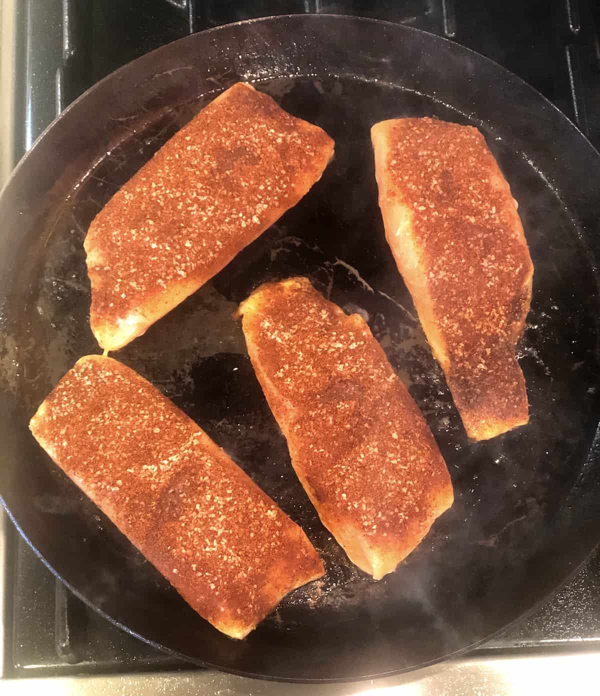 Salmon fillets being cooked in a frying pan.
