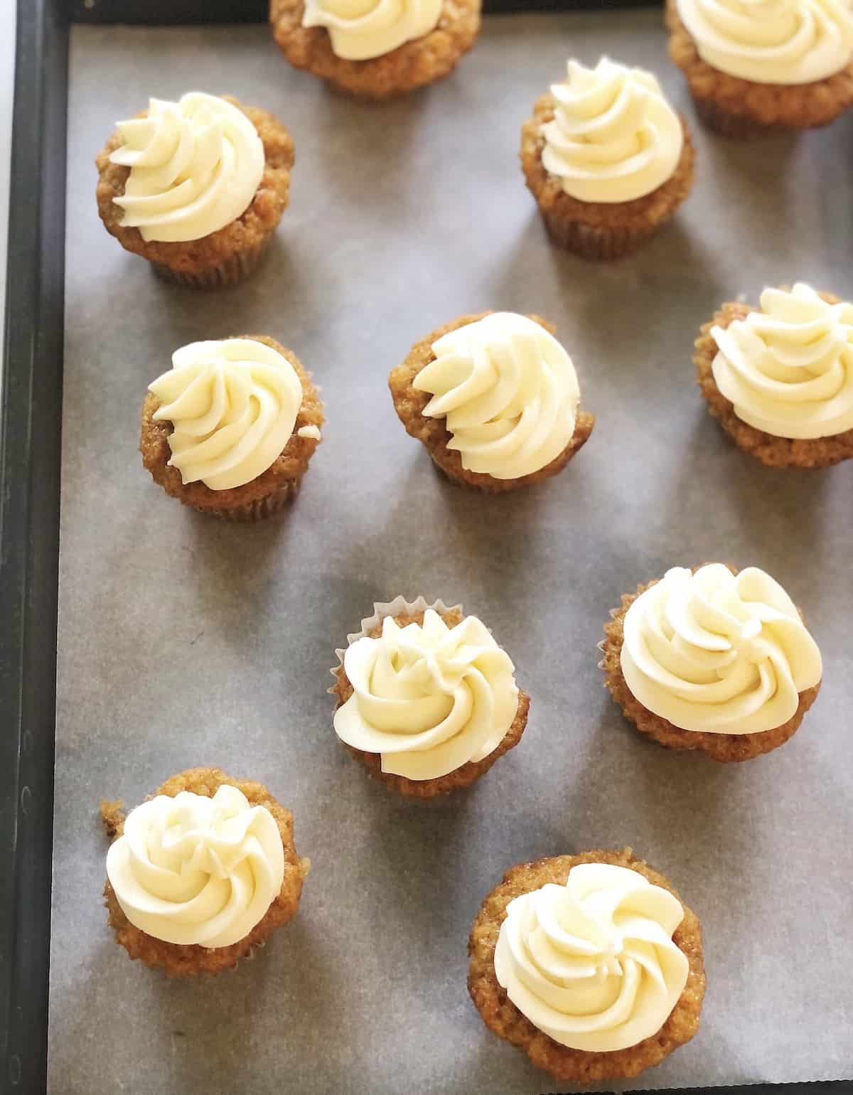 Carrot cake cupcakes with frosting on a baking sheet.