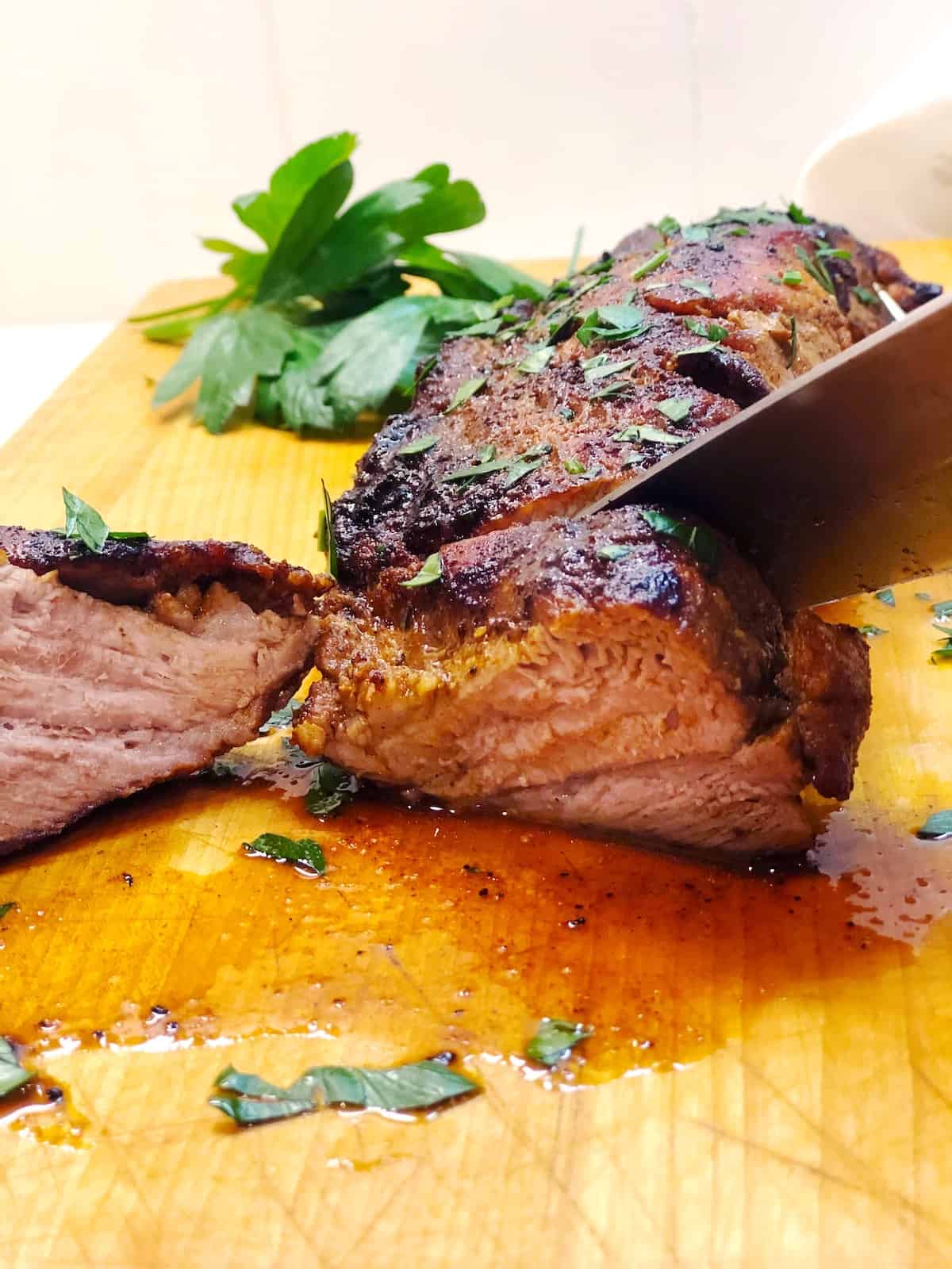 A knife is slicing a piece of pork tenderloin. 