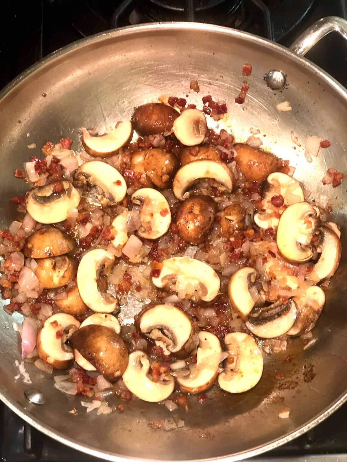 Mushrooms and onions in a pan on the stove.