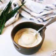 A bowl of tahini yogurt sauce with a spoon next to it.