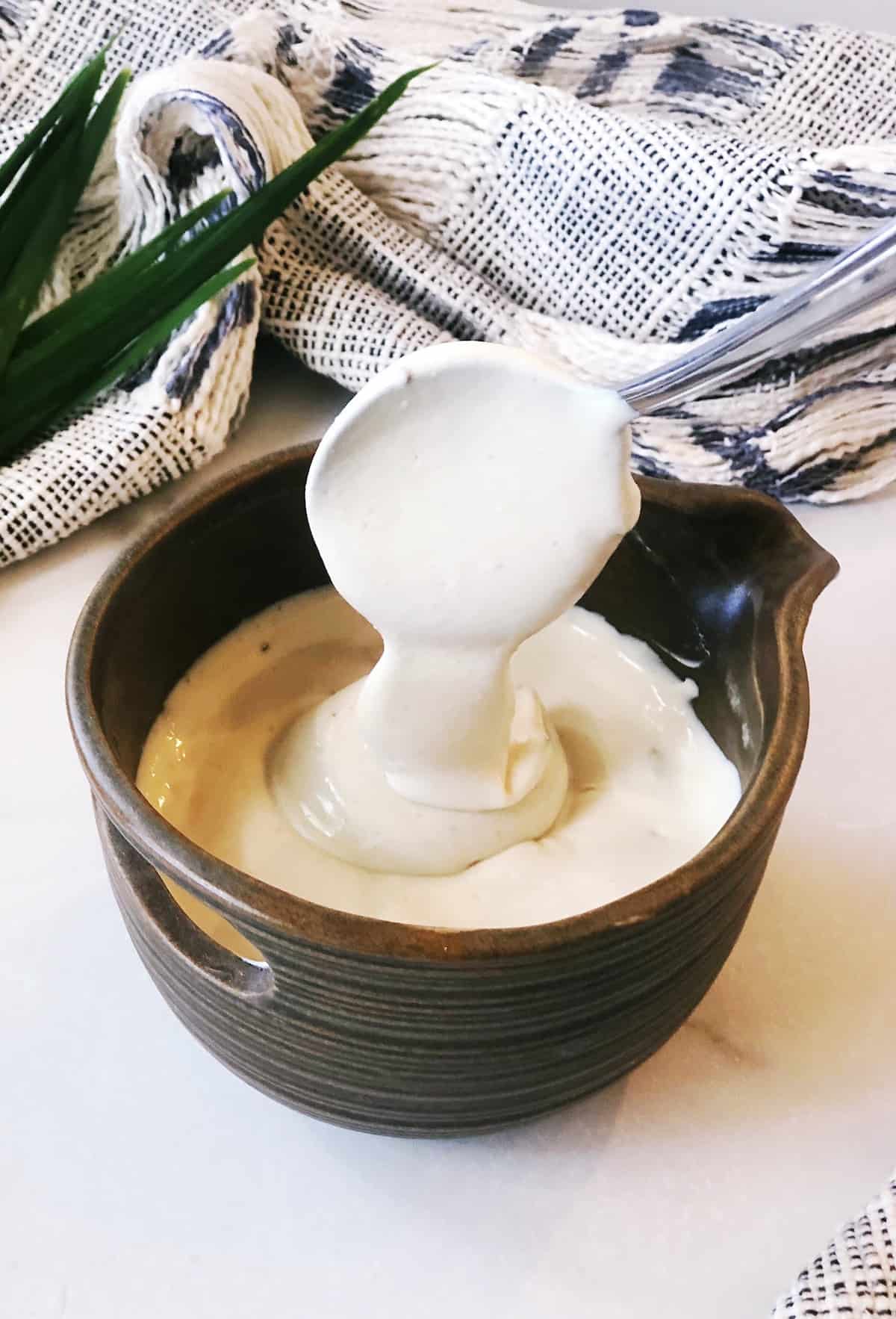A bowl of yogurt sauce with tahini with a spoon in it.