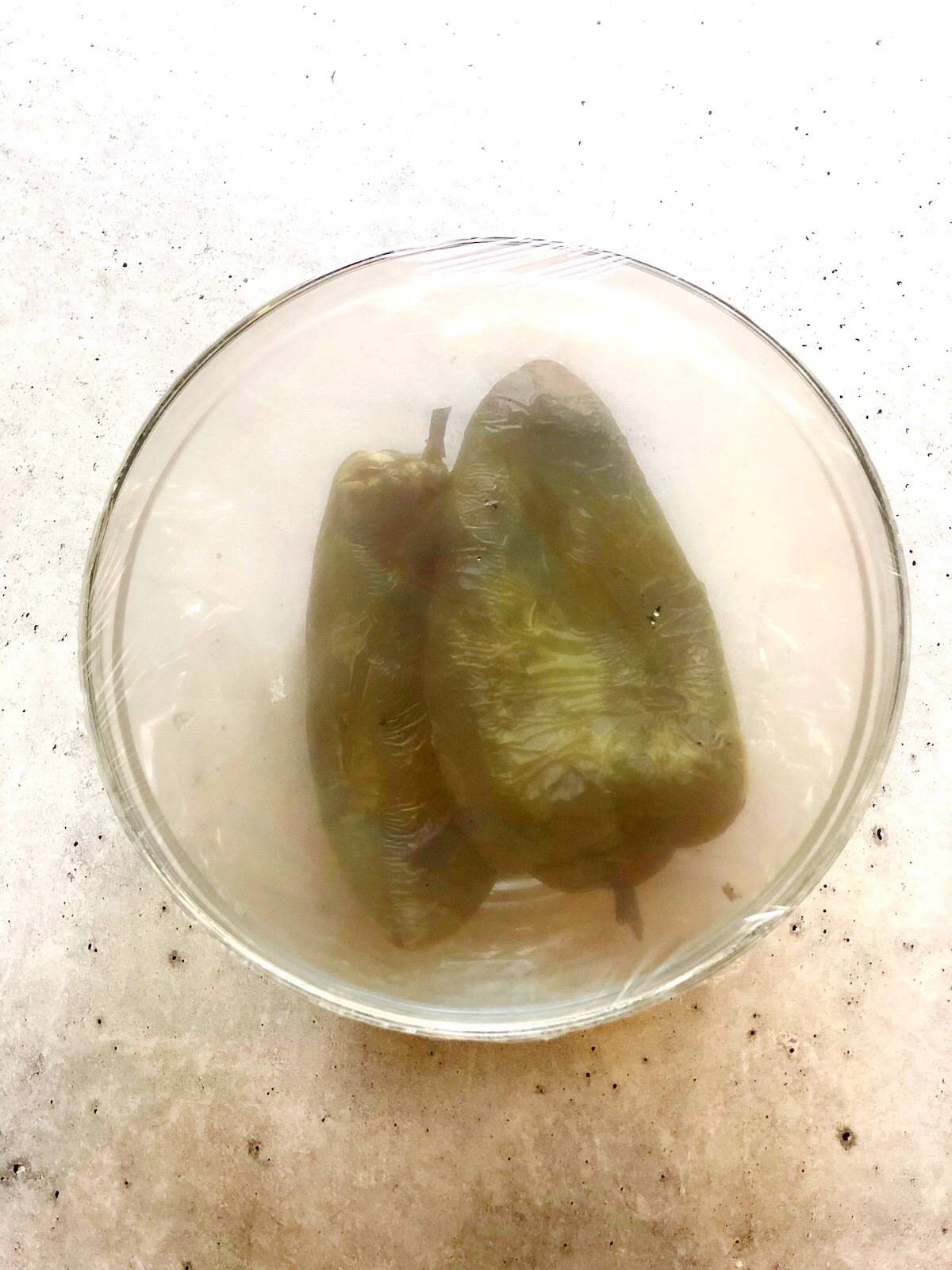 roasted poblano peppers in a bowl with a cover on top