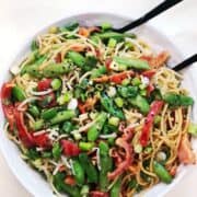 peanut pasta veggie salad in white bowl with serving spoon