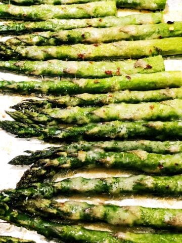 Roasted asparagus with melted cheese on top on a sheet pan.
