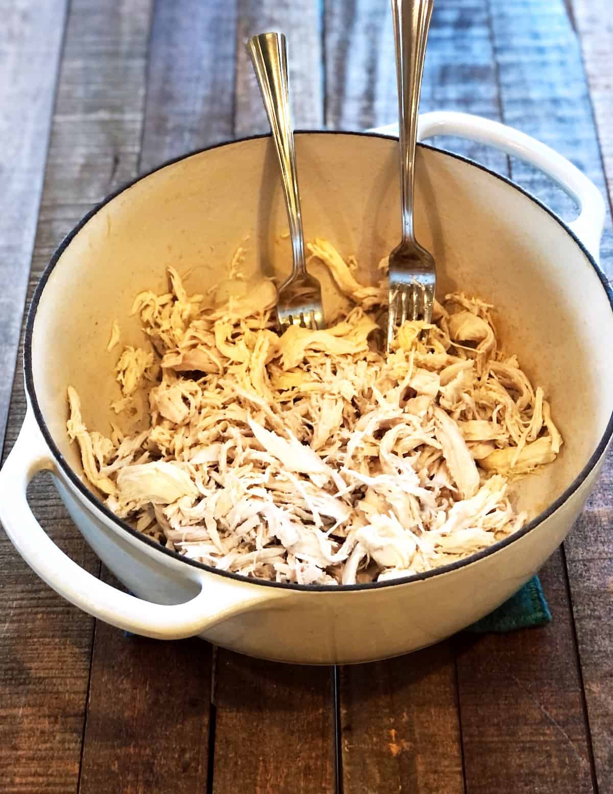 Shredded chicken in a Dutch oven on a wood board.