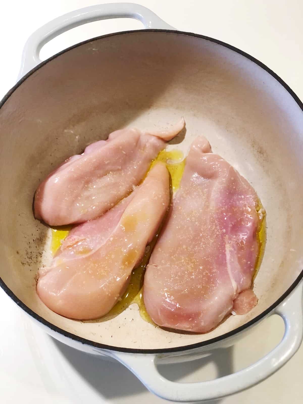 Raw chicken breasts with olive oil in a Dutch oven.